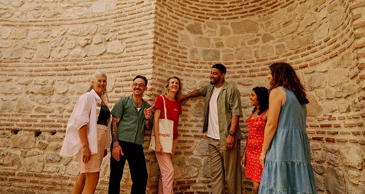 Pequeño grupo de turistas riendo junto a una antigua pared de ladrillo con textura