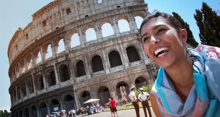Smiling traveller with scarf poses in front of Rome’s colossal Colosseum on a sunny day.