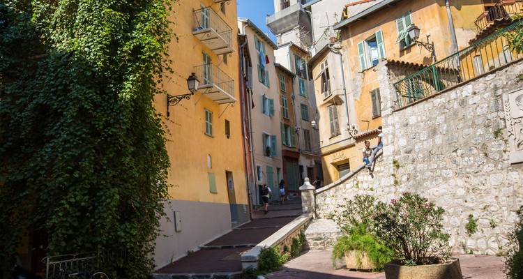 Charming narrow lane in Nice’s old town with colourful facades draped in lush greenery and balconies.