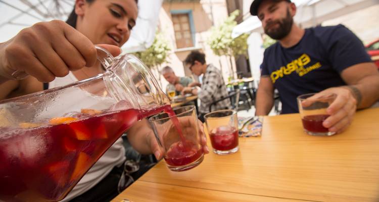 Friends pour vibrant red sangria into glasses at an outdoor Spanish café table.