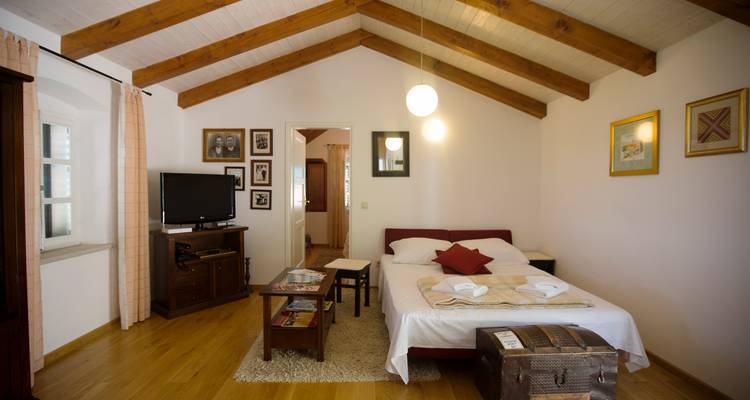 Ruim zolderslaapkamer met houten balken, televisie en ingelijste foto's aan de muur.
