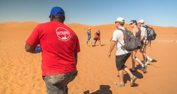Un grupo de turistas caminando por la arena con un guía en el desierto.