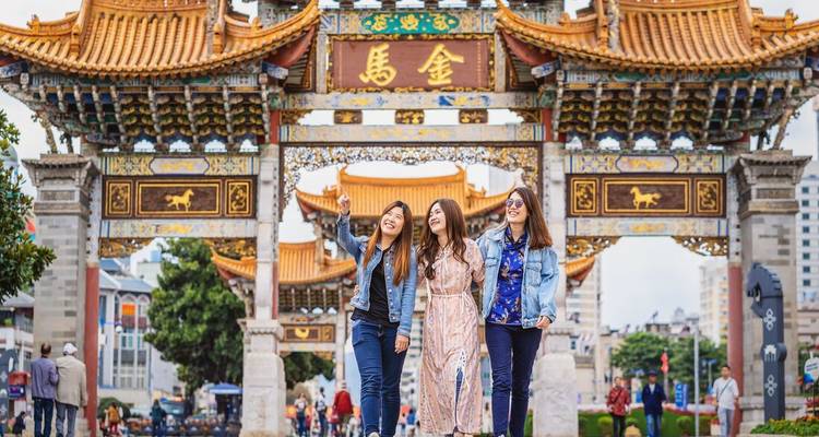 Tres amigos posando alegremente bajo una ornamentada puerta tradicional de la ciudad.