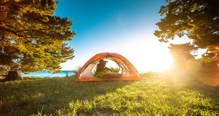 Kampeeropstelling bij een meer met een stel in een tent tijdens de zonsondergang.