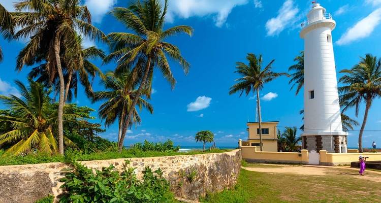 Galle lighthouse with palm trees under a blue sky