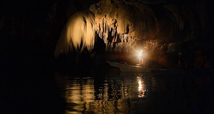 Exploración de cueva en bote, iluminada por una linterna.