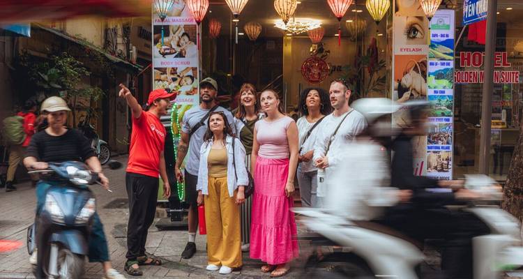El grupo de turismo está de pie afuera de una tienda colorida mientras el tráfico pasa borroso en una calle de Hanoi