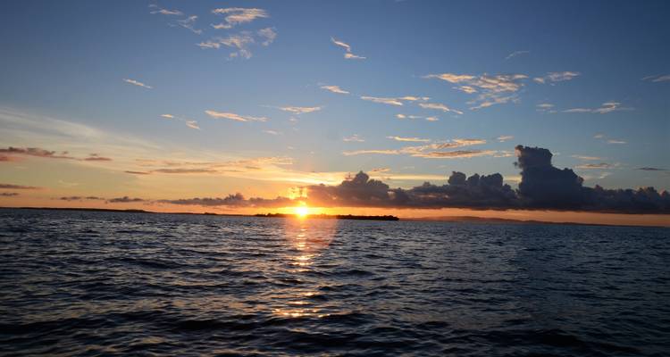 Un coucher de soleil vibrant projette une lumière dorée sur les eaux calmes de la mer et une île basse lointaine.