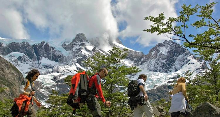 Les randonneurs avec des sacs à dos cheminent à travers les terres arbustives vers les sommets spectaculaires enneigés et les glaciers de Torres del Paine.