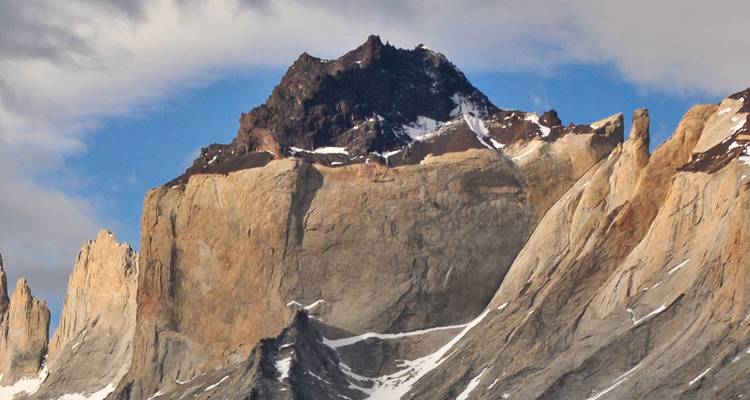 Gros plan des parois de granit translucide et des crêtes enneigées des Cuernos del Paine sous un ciel partiellement nuageux.