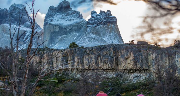 Les pics enneigés des Torres del Paine s'élèvent au-dessus d'une ligne de falaises spectaculaire, avec des randonneurs admirant la vue en contrebas.