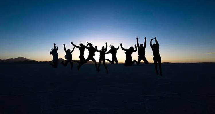 Siluetas de personas saltando en el aire con montañas al atardecer.