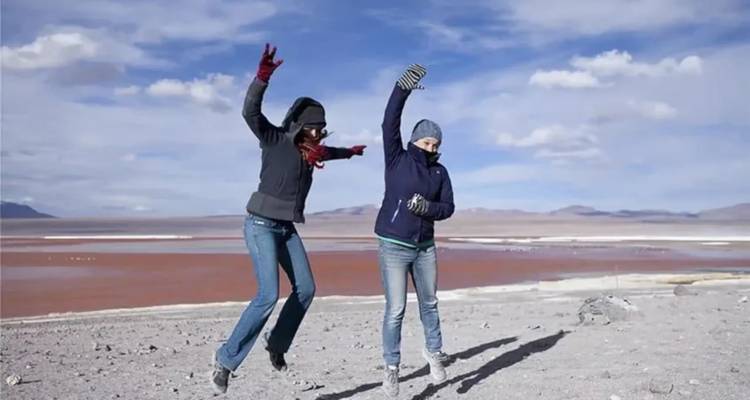 Dos personas vestidas con ropa de invierno jugando cerca de una laguna colorida.