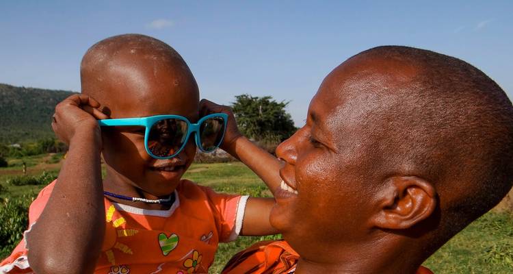 Adulte souriant tenant un enfant qui porte des lunettes de soleil.