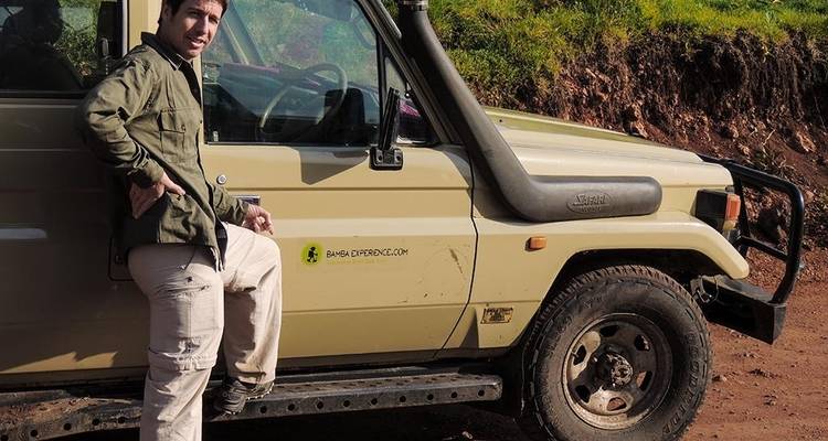 Un hombre parado junto a un vehículo de safari en un lugar polvoriento al aire libre.
