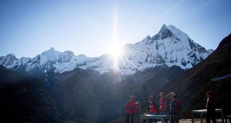 El grupo de trekking saluda el amanecer mientras el sol asoma por los picos nevados del Himalaya