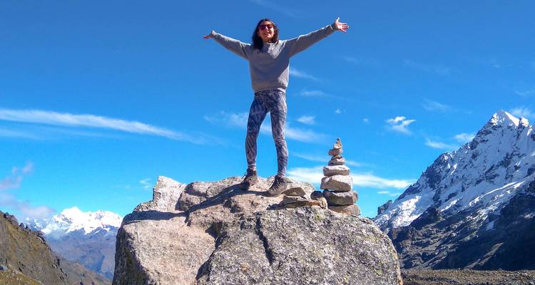 Mujer de pie sobre una roca con los brazos levantados cerca de las montañas de los Andes.