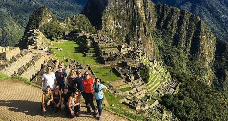 Un grupo de personas paradas frente a una antigua ciudad de piedra construida sobre una cresta montañosa.