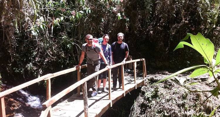 Personas de pie en un pequeño puente de madera en un área boscosa.