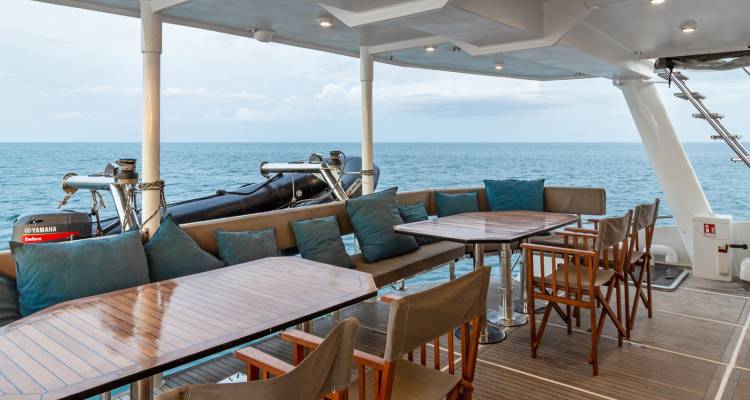 Eetgedeelte van de jacht met houten tafels en stoelen met uitzicht op open water.