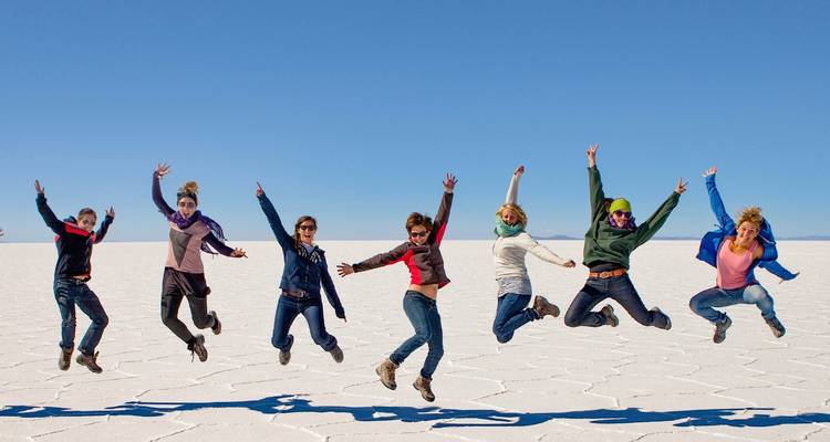 Un grupo de personas saltando en el Salar de Uyuni bajo un cielo azul despejado.
