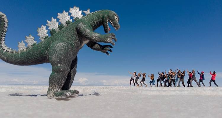 Un grupo de personas posando a lo lejos con un dinosaurio de juguete en un salar.