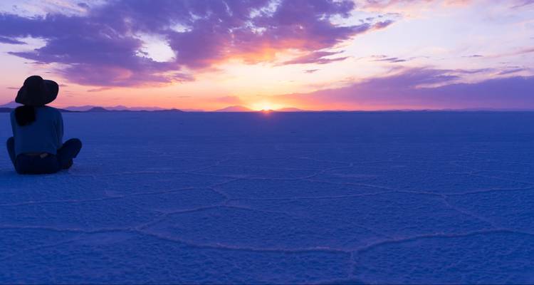Reisender, der auf der ausgedehnten sechseckigen Salzkruste von Uyuni sitzt und einen lebhaften purpur-orangen Sonnenuntergang beobachtet.