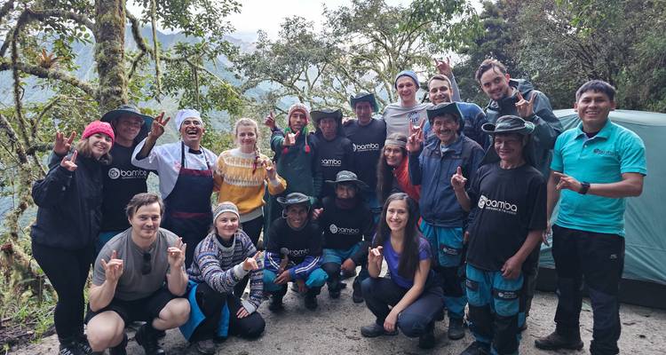 Un grupo de senderismo sonriente posa junto en un campamento en la nube-bosque a lo largo del Camino Inca con montañas brumosas de fondo.