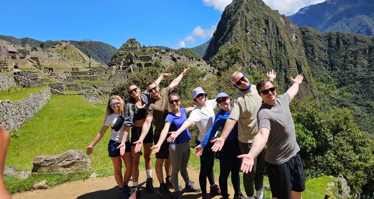 Los viajeros felices posan con los brazos abiertos en el clásico mirador de Machu Picchu bajo un cielo azul brillante.