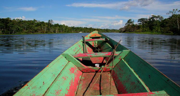 Aussicht vom Bug eines verwitterten Holzkanus, das einen breiten Amazonas-Fluss unter blauem Himmel hinabgleitet