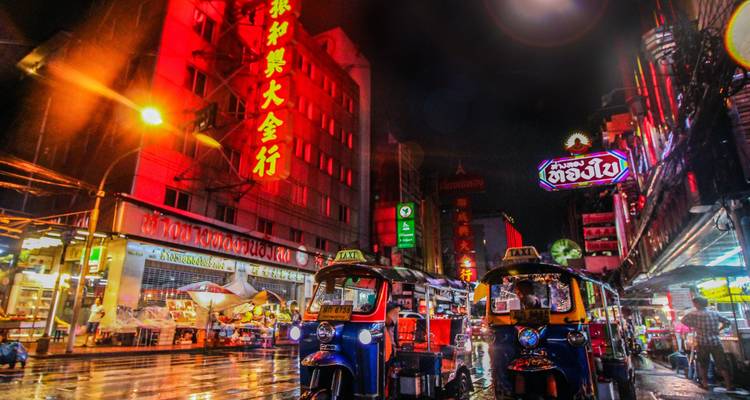 Rue de ville animée avec des tuk-tuks et des néons la nuit.