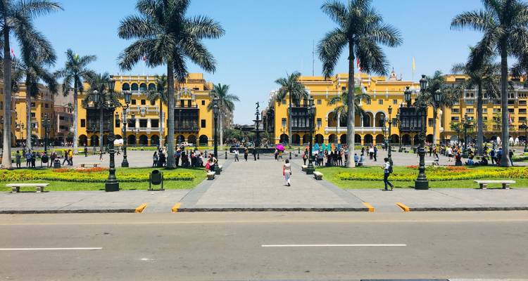 La Plaza de Armas de Lima, bordée de bâtiments coloniaux jaune vif, de palmiers et de foules se promenant au soleil.