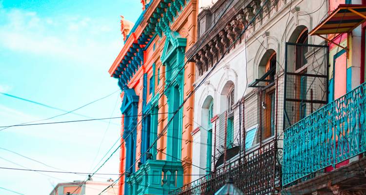 Des bâtiments historiques aux couleurs éclatantes avec des balcons en fer forgé et des câbles aériens sur une rue ensoleillée.