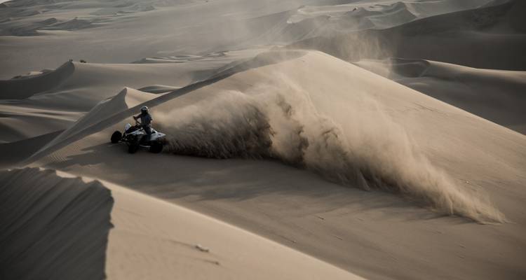 Un cavalier de VTT se précipite à travers une dune du désert en soulevant un panache de sable spectaculaire dans les airs.