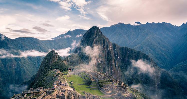 Vista aérea icónica de las ruinas de Machu Picchu envueltas en niebla con el imponente pico de Huayna Picchu detrás.
