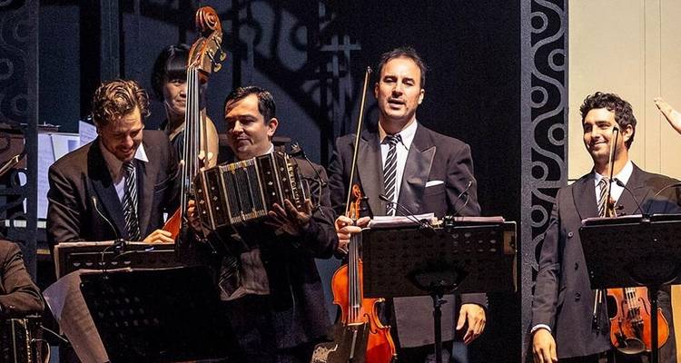 Ensemble orchestral en costumes sombres exécutant de la musique traditionnelle argentine sur scène.