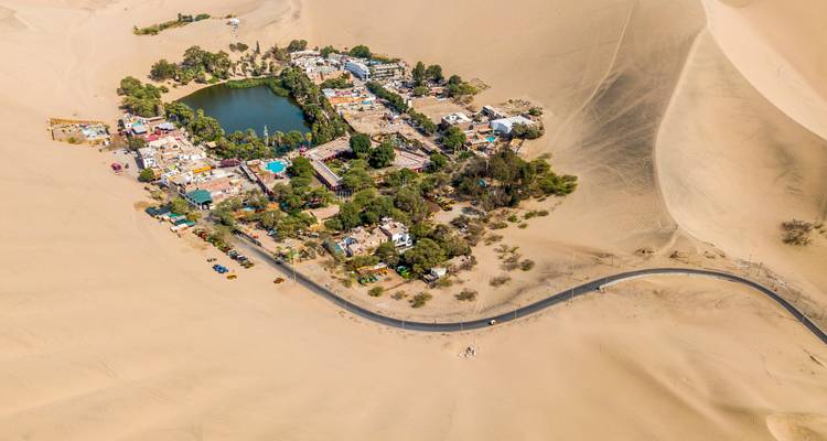 Luchtfoto van het oasisdorpje Huacachina omgeven door uitgestrekte golvende zandduinen.