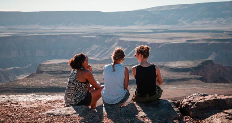 Tres personas sentadas en el borde de un cañón contemplando la vista.