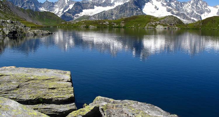 Lac alpin cristallin reflétant des pics enneigés et déchiquetés sous un ciel bleu éclatant.