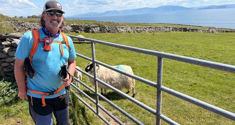 A man standing near a gate with a sheep in the background.