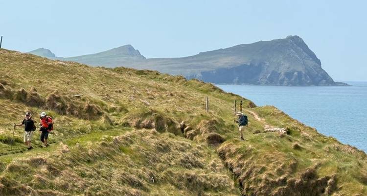 Hikers walking along a coastal path, with cliffs and sea visible.