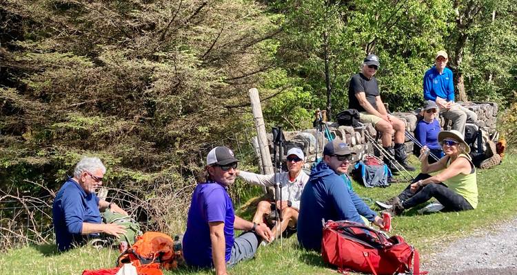 Hikers taking a break and sitting on grass, with trees in the background.