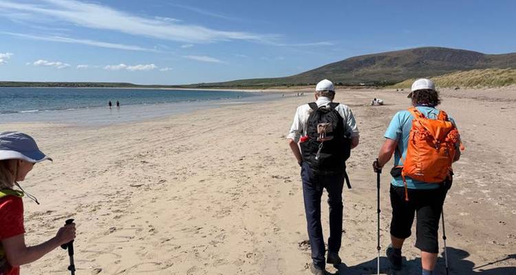 Des gens marchant sur une plage de sable avec des collines en arrière-plan.