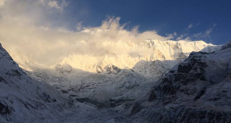 Schneebedeckte Berge mit Wolkendecke und wechselnder Beleuchtung.