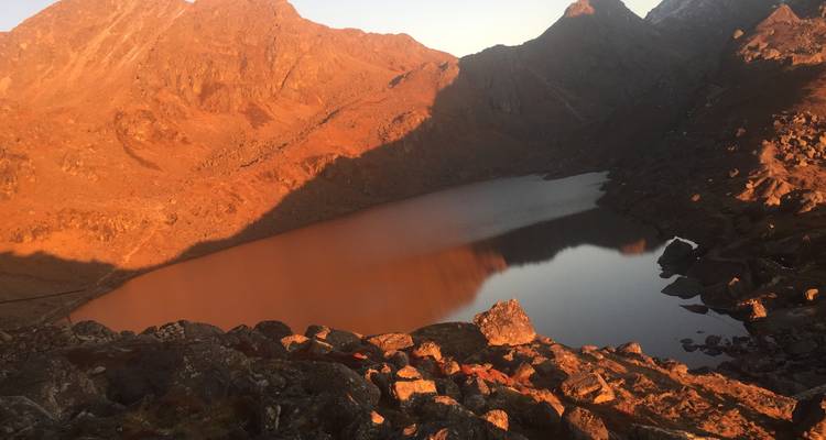 Lago rodeado de montañas con tonos rojizos durante la puesta de sol.