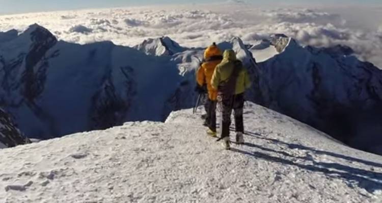 Twee mensen in klimuitrusting op een besneeuwde bergtop.