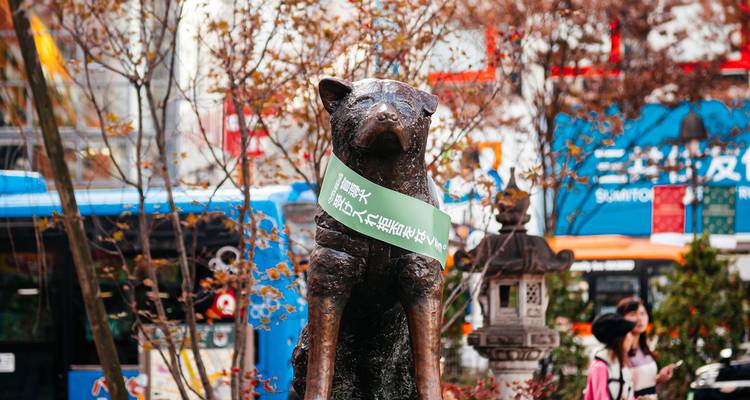 Statue d'un chien avec une écharpe verte dans un cadre urbain animé.