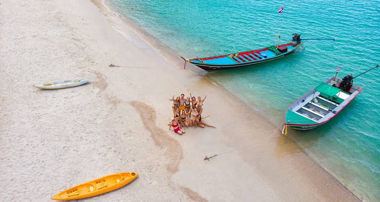Escena de playa con botes y un grupo de personas saludando a la cámara.