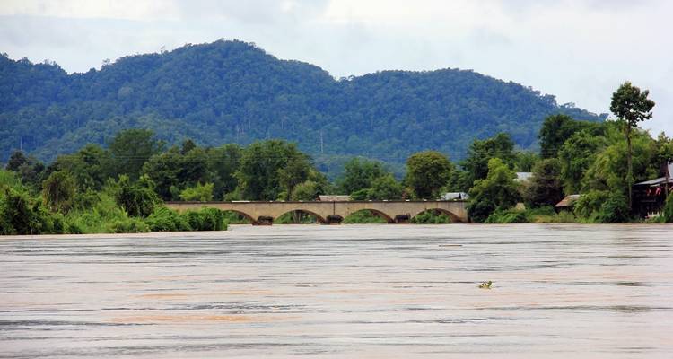 Río ancho con un puente y colinas boscosas al fondo.
