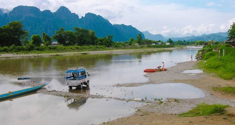 Río con botes pequeños y gente cerca de una cordillera.